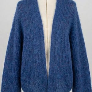 K&ouml;nnte beinhalten: Ein blauer Cardigan, der auf einer Schaufensterpuppe pr&auml;sentiert wird. Der offene Pullover hat lange &Auml;rmel und ist aus einem weichen, strukturierten Material gefertigt. Die Farbe ist ein tiefes Blau. Der Cardigan ist ein stilvolles Kleidungsst&uuml;ck.