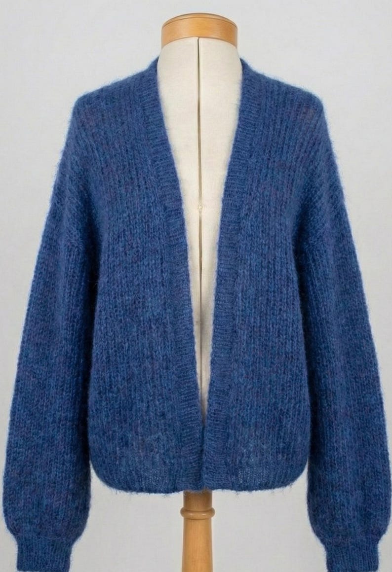 K&ouml;nnte beinhalten: Ein blauer Cardigan, der auf einer Schaufensterpuppe pr&auml;sentiert wird. Der offene Pullover hat lange &Auml;rmel und ist aus einem weichen, strukturierten Material gefertigt. Die Farbe ist ein tiefes Blau. Der Cardigan ist ein stilvolles Kleidungsst&uuml;ck.