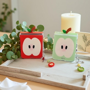 Puede incluir: Dos impresoras portátiles, una roja y otra verde, cada una diseñada para parecerse a una manzana. El diseño de la manzana incluye un corazón blanco con puntos negros para las semillas y un tallo marrón. La palabra "APPLE" está impresa en cada impresora.