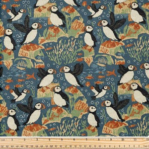 May include: A patterned fabric featuring puffins, fish, and aquatic plants. The design includes various puffin poses, set against a blue background with orange and green accents. The fabric has a repeating pattern with a ruler at the bottom.