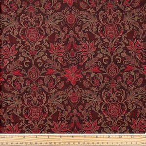 Pode incluir: Close-up de um tecido com um padrão floral repetido em tons de vermelho e dourado. O design apresenta flores estilizadas, folhas e volutas sobre um fundo vermelho escuro. O tecido é medido com uma régua em cm.