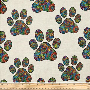 Könnte beinhalten: Stoff mit einem sich wiederholenden Muster aus farbenfrohen Pfotenabdrücken. Jeder Pfotenabdruck ist mit aufwendigen Blumen- und Paisley-Designs in Blau-, Grün-, Rot- und Gelbtönen gefüllt. Der Hintergrund ist hellbeige.