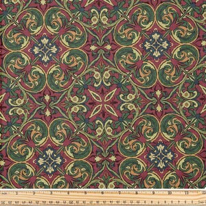 Könnte beinhalten: Nahaufnahme eines Stoffes mit einem sich wiederholenden Muster. Das Muster zeigt einen burgunderfarbenen Hintergrund mit grünen, goldenen und blauen floralen und scrollartigen Motiven. Unten befindet sich ein Lineal mit cm-Maßen.