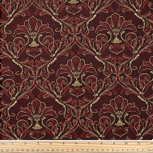 Pode incluir: Tecido bordô com um padrão repetitivo de motivos florais e foliares estilizados em tons de vermelho e dourado. O design apresenta arranjos simétricos com uma aparência texturizada, adequado para estofados ou projetos decorativos. Uma régua está na parte inferior.