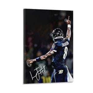 May include: A framed print featuring a football player in a black and purple uniform, with the number 8 visible. The player is raising his arm, and the image includes the player's signature. The word "RAVENS" is visible on the helmet.