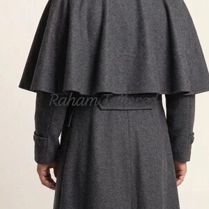 May include: A charcoal gray wool coat with a cape-like shoulder design. The long coat features a belt at the waist and buttoned cuffs. The text "Raham Tailors" is visible on the back of the coat.