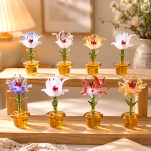 May include: Eight miniature glass flower figurines in amber-colored pots. Each piece features a green stem and a uniquely shaped, multi-colored glass blossom in shades of blue, pink, orange, white, purple, red, and yellow, arranged on a wooden stand.