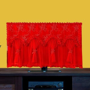 以下が含まれることがあります： 鮮やかな赤色のテレビカバー。繊細な花の刺繍とスカラップの縁取りが施されています。カバーはシアー生地で作られており、装飾的なリボン留めが付いています。テレビに被せて、エンターテイメントエリアに装飾的なアクセントを加えるように設計されています。
