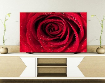 May include: A close-up of a vibrant red rose with water droplets, displayed on a large screen. The image is a high-resolution photograph, showcasing the intricate details of the flower's petals. The screen is set on a white and wood-toned cabinet.