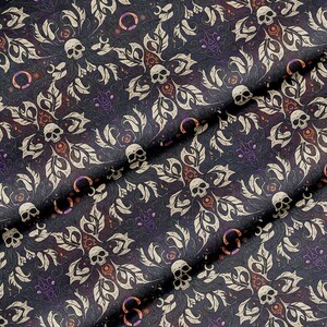 May include: Dark fabric with a repeating pattern of skulls, leaves, and floral elements in cream, orange, and purple. The background is a deep navy blue, creating a gothic or Halloween theme.