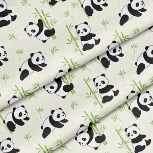 May include: Cream-coloured fabric featuring a repeating pattern of black and white panda bears, green bamboo, and small green leaves. The pandas are in different poses, some climbing bamboo.