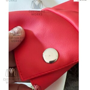 May include: Close-up of a red leather item with a silver button. The item is stitched and has a smooth texture. The text "CUSTOM FIT WORKS" is printed on the item in white.