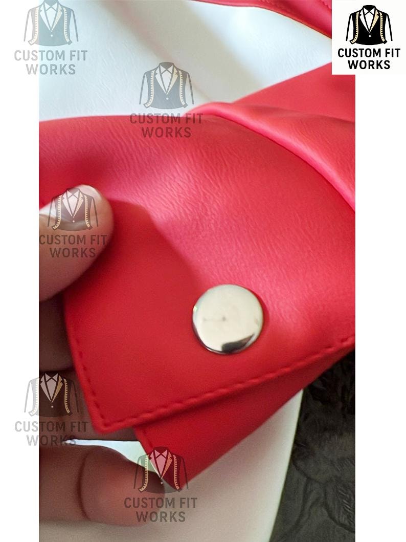 May include: Close-up of a red leather item with a silver button. The item is stitched and has a smooth texture. The text "CUSTOM FIT WORKS" is printed on the item in white.