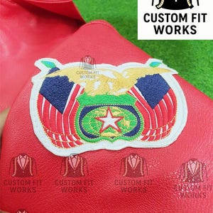 May include: Close-up of a red leather item with an embroidered patch featuring a star, eagle, and flag design. The patch is surrounded by a white border. The text "CUSTOM FIT WORKS" is visible.