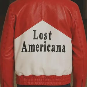 May include: Red and white leather jacket with the text "Lost Americana" on the back. The jacket has a classic bomber style with a ribbed hem and cuffs. The design features a bold color block pattern.