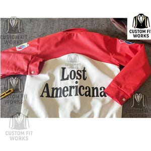 May include: A red and white jacket with the text "Lost Americana" in black. The jacket has red sleeves and shoulders, with a white body. The sleeves have buttoned cuffs. The jacket is from Custom Fit Works.