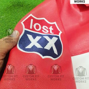 May include: Close-up of a red leather jacket with a white and blue embroidered patch that reads "lost" above the letters "XX". The jacket has the text "CUSTOM FIT WORKS" printed on it.
