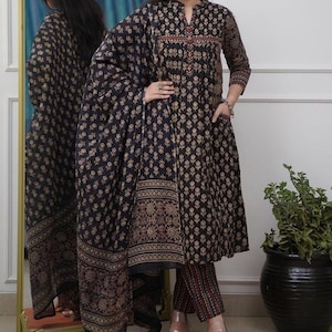 Op de afbeelding: Een zwart en goud bloemenprint driedelig outfit. De outfit bestaat uit een tuniek met lange mouwen, een bijpassende broek en een sjaal. De tuniek heeft een mandarijnkraag en een knoopsluiting. De broek heeft een slanke pasvorm. De sjaal heeft een decoratieve rand.