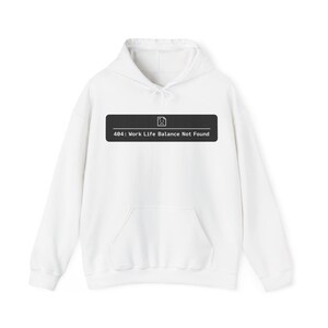 Puede incluir: Sudadera con capucha blanca con bolsillo delantero y capucha con cordón. Un rectángulo negro en la parte delantera muestra el texto "404: Work Life Balance Not Found" en blanco, con un pequeño icono encima.