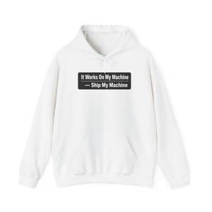 Op de afbeelding: Witte hoodie met een voorzak en trekkoord. De voorkant van de hoodie heeft een zwarte rechthoek met de tekst "It Works On My Machine" boven "- Ship My Machine".