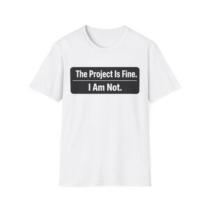 Puede incluir: Camiseta blanca con cuello redondo y mangas cortas. La camiseta presenta un diseño rectangular negro con el texto "The Project Is Fine. I Am Not." en blanco, centrado en el pecho.