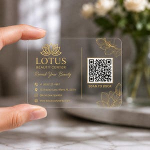 May include: A rectangular transparent business card featuring gold text and graphics. It displays the Lotus Beauty Center logo, the text Reveal Your Beauty, contact details, and a QR code with the text SCAN TO BOOK, accented by gold floral line art.