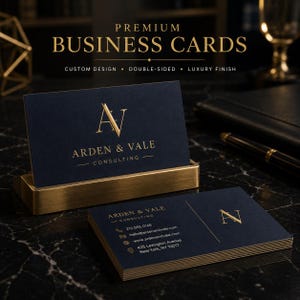 Op de afbeelding: Een set marineblauwe visitekaartjes met goudfolie belettering en logo's. Eén kaart staat in een gouden metalen houder, terwijl een stapel plat ligt. De kaarten bevatten de tekst Arden & Vale Consulting en een adres in New York.