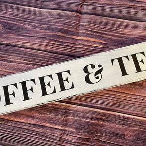 May include: White wooden sign with black lettering that reads "COFFEE & TEA" on a brown wood background.