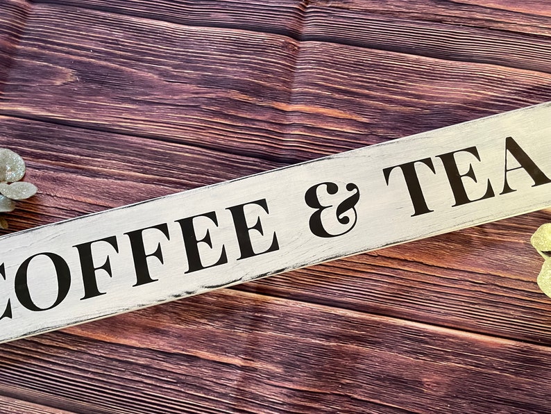 May include: White wooden sign with black lettering that reads "COFFEE & TEA" on a brown wood background.