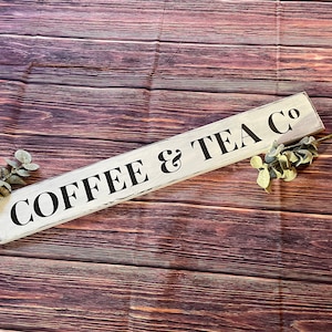 May include: A white wooden sign with black lettering that reads "COFFEE & TEA CO" on a brown wood background.