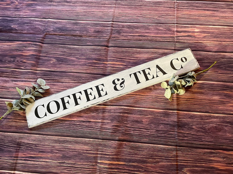 May include: A white wooden sign with black lettering that reads "COFFEE & TEA CO" on a brown wood background.