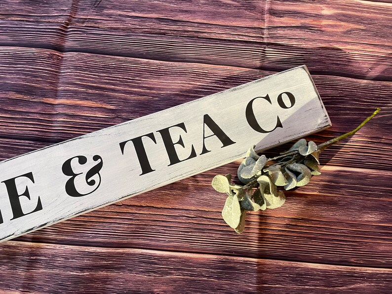 May include: White wooden sign with black text that reads "Cake & Tea Co.". The sign is on a brown wooden background.