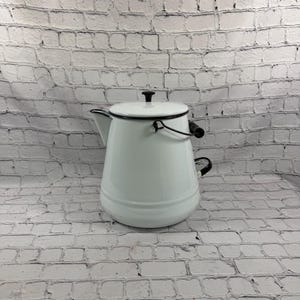 May include: A white enamel coffee pot with a black rim, a black lid knob, and a black side handle. The pot features a metal bail handle with a black grip and a tapered spout. The exterior finish is smooth and glossy, contrasting with the dark hardware.