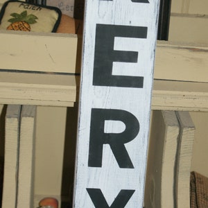 May include: A white wooden sign with black painted letters spelling "KERRY". The sign has a distressed, weathered look.