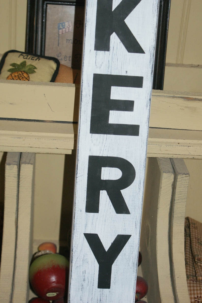 May include: A white wooden sign with black painted letters spelling "KERRY". The sign has a distressed, weathered look.