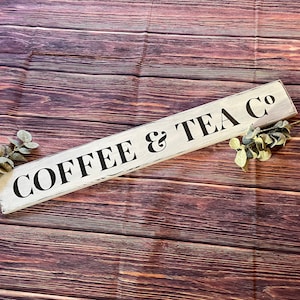 May include: White wooden sign with black lettering that reads "COFFEE & TEA CO" on a brown wood background.