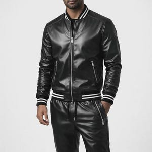May include: Black leather bomber jacket with white stripes on the collar, cuffs, and waist. The jacket has a zipper closure and two side pockets. Matching black leather pants with a drawstring waist and zippered pockets complete the outfit.