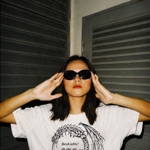 Op de afbeelding: Wit T-shirt met een zwart-wit drakenontwerp en de tekst "SenLinVu? oh she ate." Het shirt heeft een ronde hals.