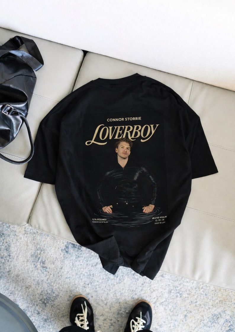 May include: Black t-shirt featuring a graphic of a man in water with the text "Loverboy" and "Connor Storrie". The shirt also includes the text "Ilya Rozanov" and "Heated Rivalry".