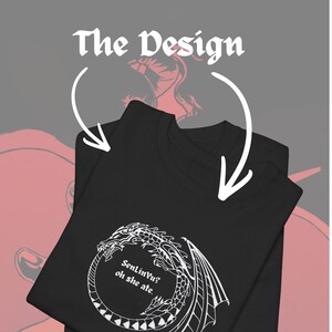 Op de afbeelding: Zwart T-shirt met een wit drakenontwerp en de tekst "SenLinVu? oh she ate." Het shirt is opgevouwen, met de tekst "The Design" erboven. Het ontwerp is een fantasie-thema grafisch.