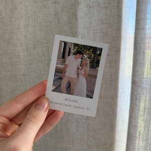 May include: A white polaroid-style photograph showing a couple outdoors. The photo includes the date 08.02.2026 and the names Kaylen & David | Appleton, WI. The photograph is held in a hand.