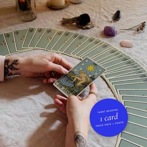 Könnte beinhalten: Ein Tarot-Kartenlesedienst mit einem Fächer aus salbeigrünen Tarotkarten, die auf einer Fläche ausgebreitet sind. Eine Karte mit dem Titel The Star wird hochgehalten und zeigt eine Figur, die unter einem großen gelben Stern an einem Becken kniet. Enthält eine blaue kreisförmige Grafik mit dem Text: Tarot Reading 1 card Voice Note + Photo.