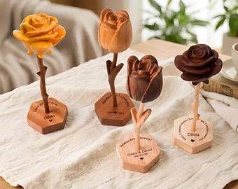 Peut inclure: Quatre sculptures de roses en bois de différentes nuances de marron et de jaune. Chaque rose est montée sur une tige et une base en bois. Les bases comportent des textes gravés, dont des noms et des dates. Les roses sont exposées sur un tissu crème.