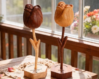 Peut inclure: Deux sculptures de tulipes en bois, une marron foncé et une marron clair, sont posées sur une table. Chaque tulipe a une tige et une base hexagonale avec du texte gravé. La tulipe marron foncé porte l'inscription "Happy Anniversary! Olivia & David 04/21/21". La tulipe marron clair porte l'inscription "Love you forever Olivia".