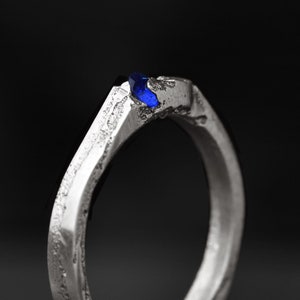 May include: A silver ring with a textured finish and a blue gemstone set in the top.