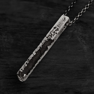 Könnte beinhalten: Eine Halskette mit einem silbernen Barren-Anhänger mit strukturierter Oberfläche. Der Anhänger ist an einer silbernen Kette befestigt.