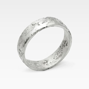 May include: A silver ring with a textured, uneven surface. The ring has a band-like design and appears to be made of metal. The ring is set against a white background. The ring is marked with "925."