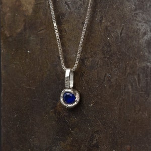 Könnte beinhalten: Eine silberne Kettenkette mit einem kleinen Anhänger mit einem dunkelblauen Edelstein.