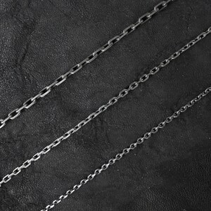May include: Four silver chains of different lengths and thicknesses on a black background.