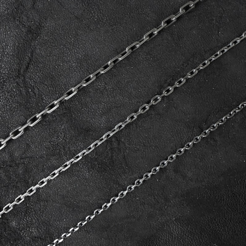 May include: Four silver chains of different lengths and thicknesses on a black background.